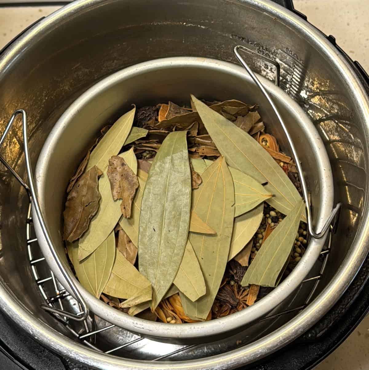 Whole aromatic spices — bay leaves, coriander, cinnamon, cardamom, and cloves — arranged in a spice grinder jar before roasting.