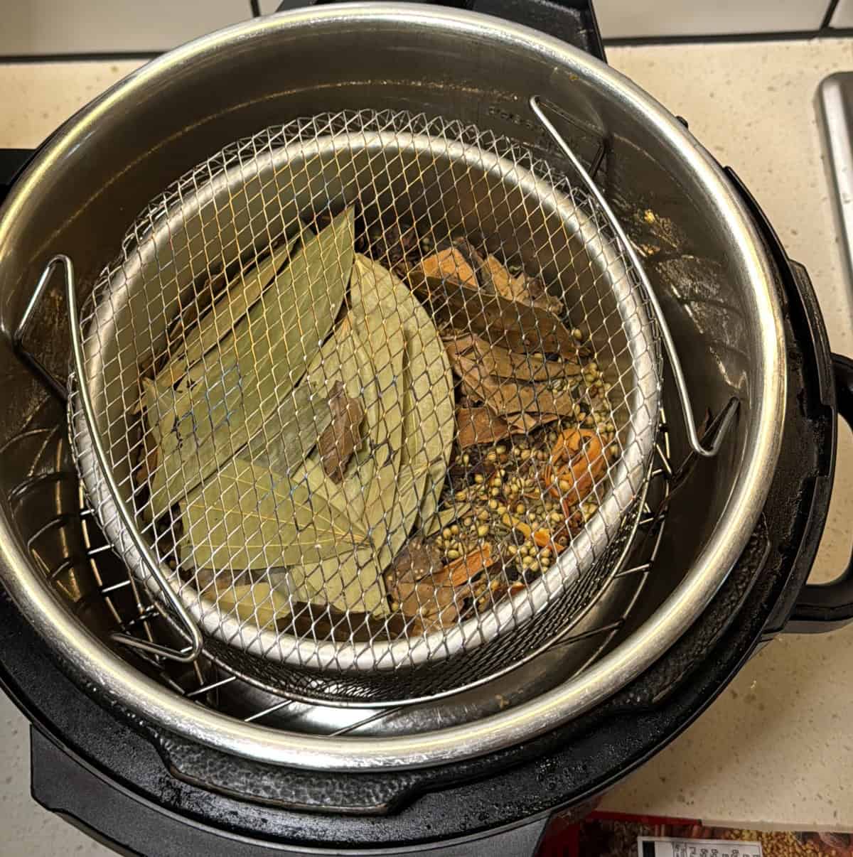 Spices placed inside an air fryer basket covered with a perforated tray for roasting.