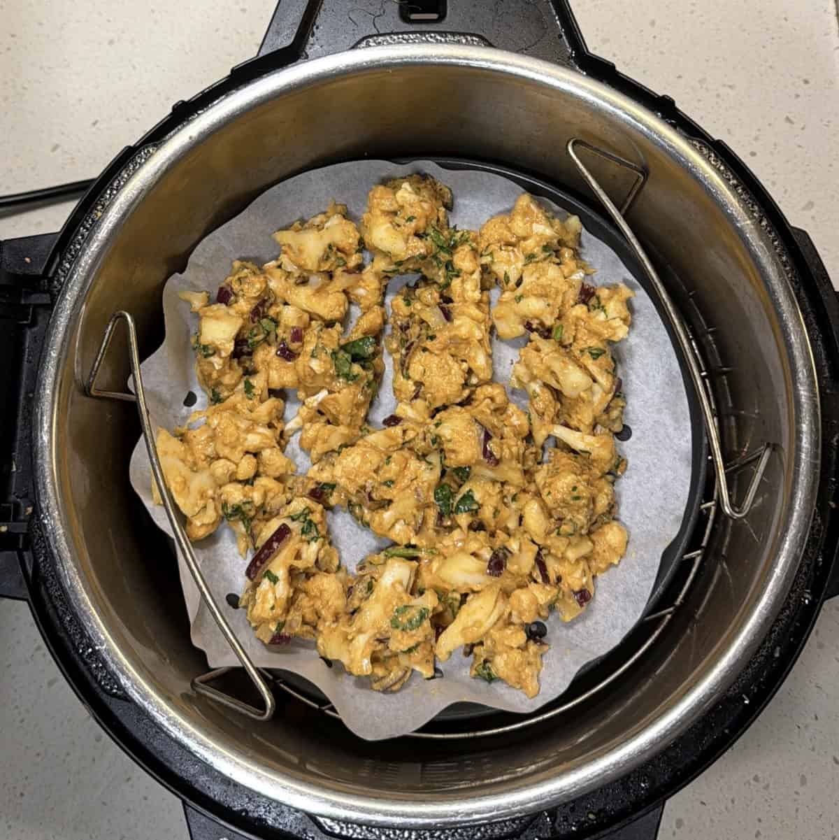 Gobi pakora mixture placed on parchment paper in air fryer basket