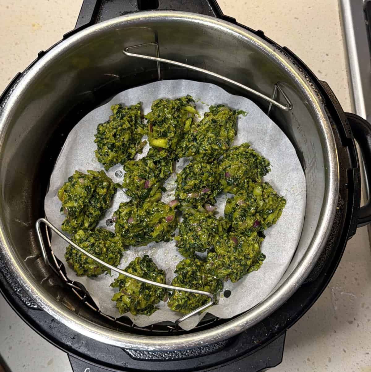 Spinach pakora mixture shaped on parchment paper in the air fryer basket