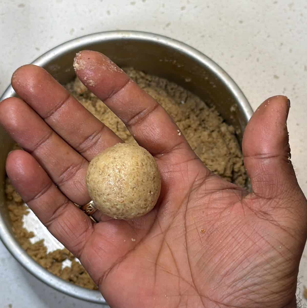 oats ladoo being shaped into a round ball by hand