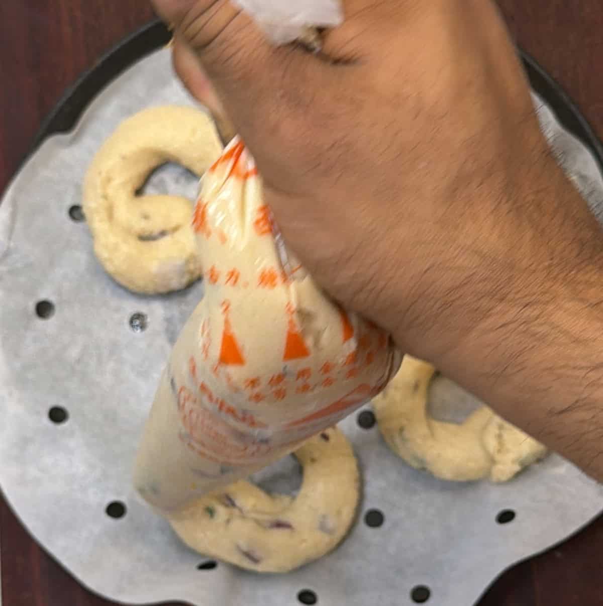 Medu vada batter being piped into rings on a perforated parchment-lined steaming tray.