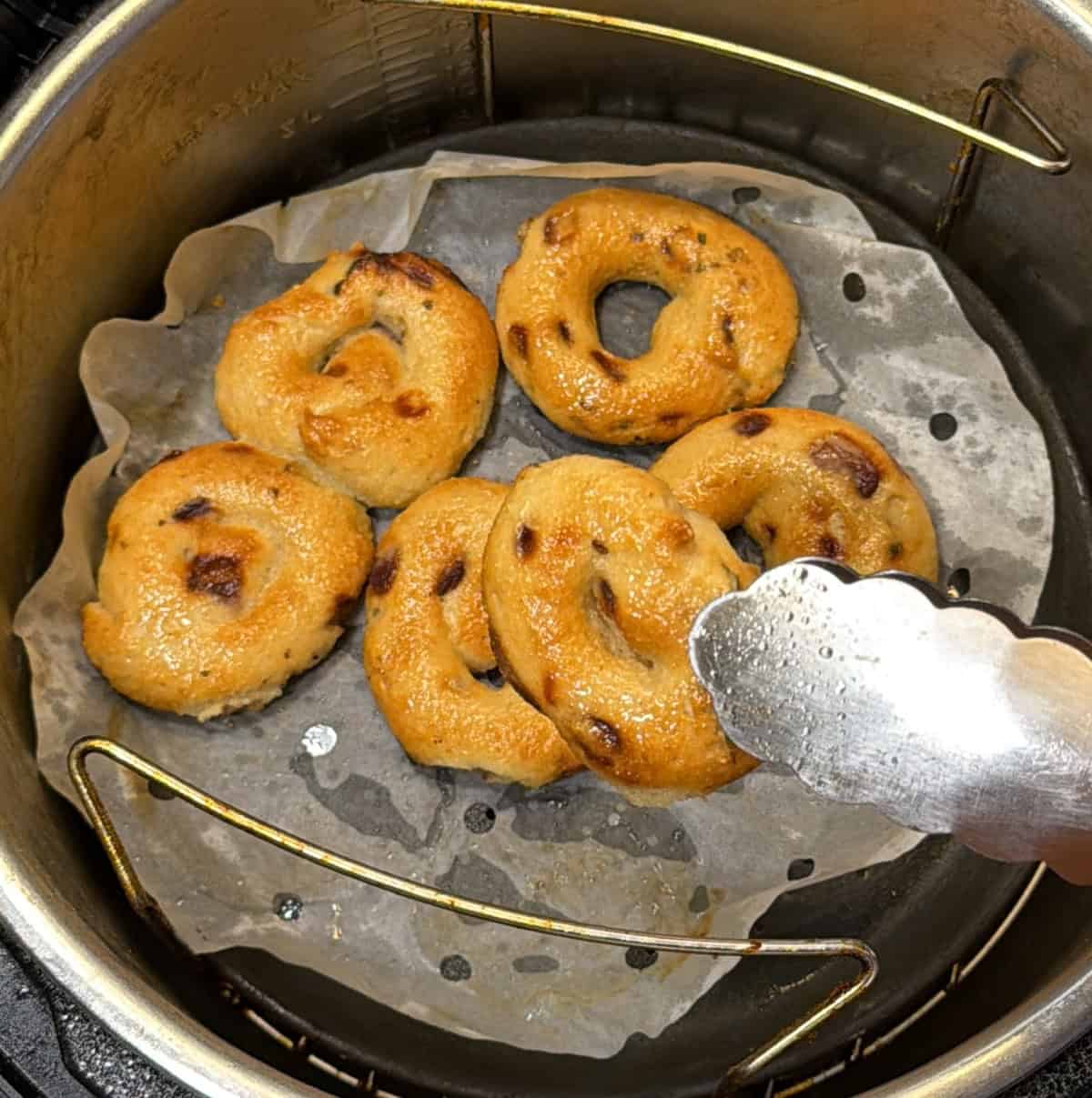 Golden-brown air fryer medu vadas being picked up with kitchen tongs.