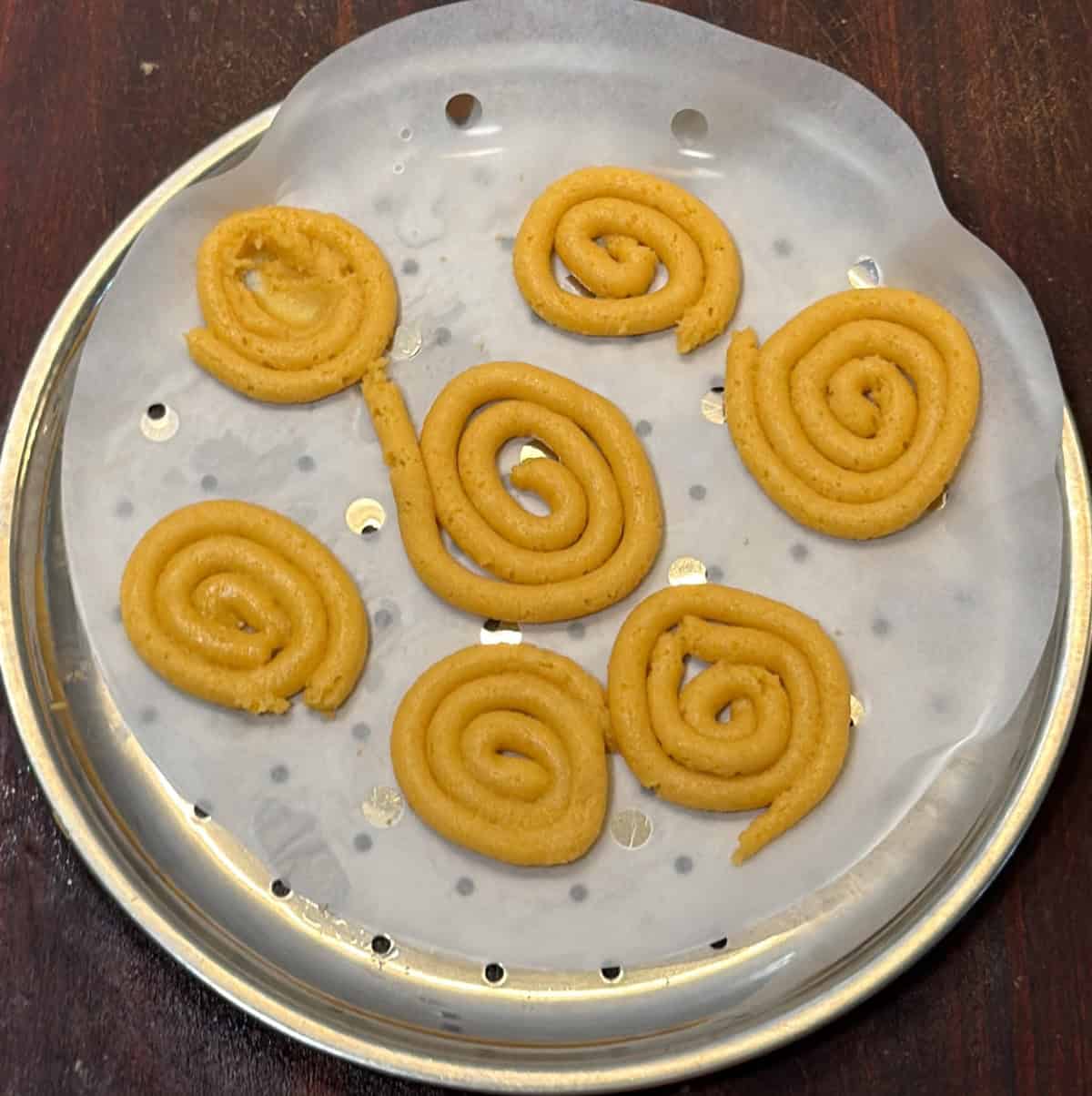 Piped jalebi spirals arranged on a steaming tray