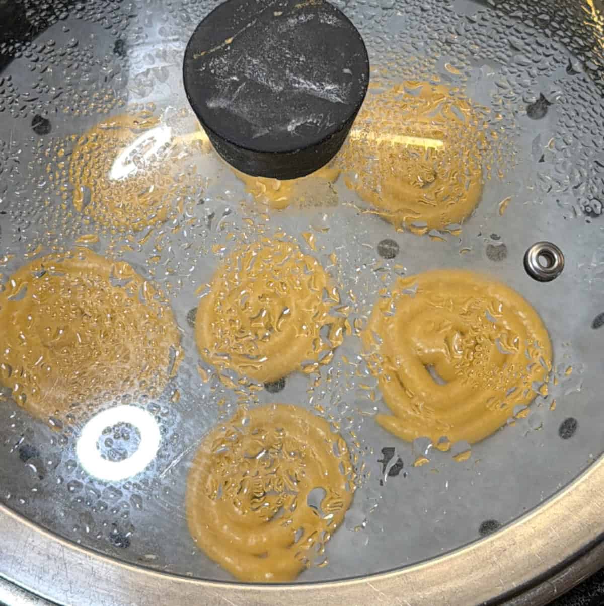 Jalebi spirals steaming under a covered lid