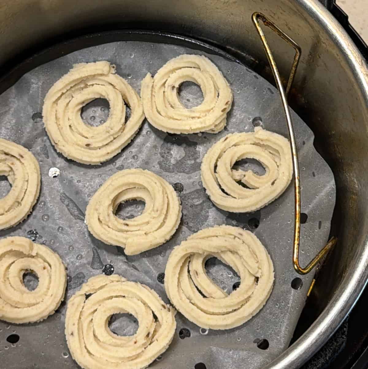 Pale uncooked murukku spirals arranged in an air fryer basket
